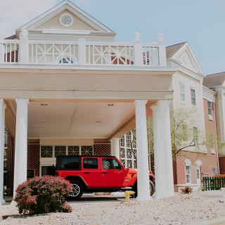 A red car parked in the driveway of a suburban house with columns.