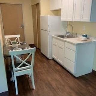 A compact kitchen and dining area with white cabinets and wooden flooring.