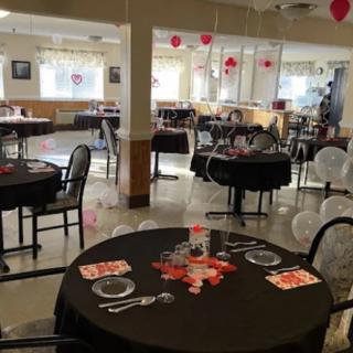 A decorated room with tables set for a Valentine's themed party, featuring red and white balloons.