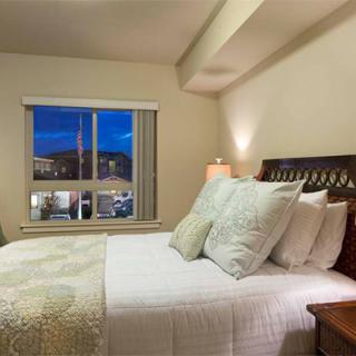 A cozy bedroom with a large bed, adorned with pillows and a bedside lamp, offering a nighttime city view from the window.