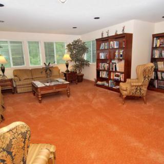 A cozy living room with bookshelves, a sofa, armchairs, and a large carpeted floor.
