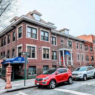 A red car parked in front of a brick building on a city street.
