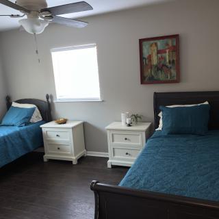 A cozy bedroom with two twin beds, blue bedding, and white nightstands next to a window.