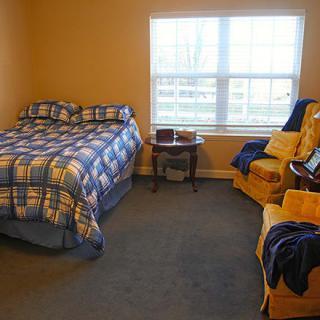 A cozy bedroom with a bed, chair, and window allowing natural light.