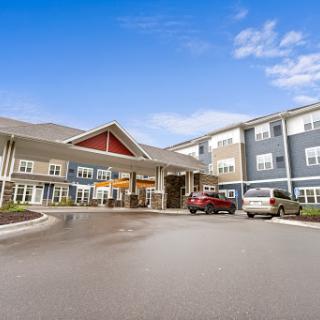 A welcoming view of a modern residential complex with a spacious entrance and outdoor parking under a clear blue sky.