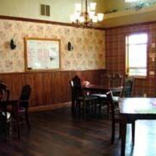 A cozy dining area with wooden tables and chairs, warm lighting, and classic wallpaper.