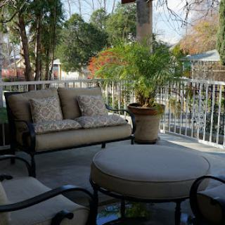 A cozy outdoor patio area featuring a comfortable couch and a coffee table, surrounded by greenery.