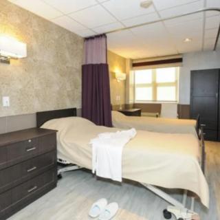 A hospital room featuring adjustable medical beds, separated by privacy curtains with essential furniture and a calming atmosphere.