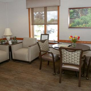 A cozy living room with armchairs, a table with chairs, a lamp, and a painting on the wall.