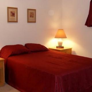 A cozy bedroom with a red bedspread, nightstand, and lamp.