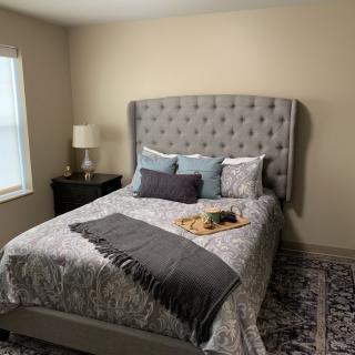 A cozy bedroom with a tufted headboard, neatly arranged pillows, and a bedside lamp.