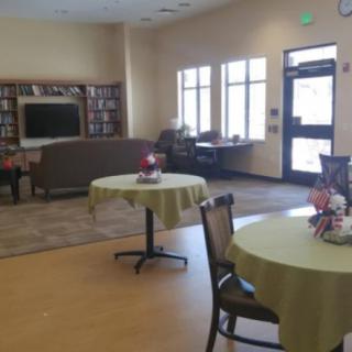 A community room with tables, chairs, and a television, surrounded by bookshelves.