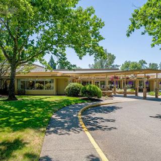 A view of a school building surrounded by trees with a driveway on a sunny day.