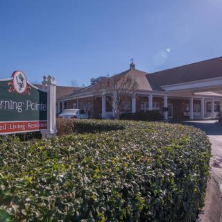 A well-maintained building entrance with a sign and lush greenery on a sunny day.