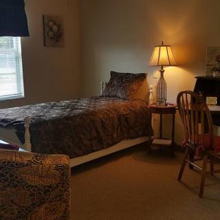 A cozy bedroom with a single bed, lamp, and desk by the window.