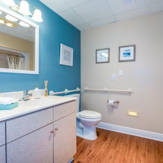 A modern bathroom with a blue accent wall, featuring a sink, mirror, and toilet, complemented by wooden flooring and decorative artwork.