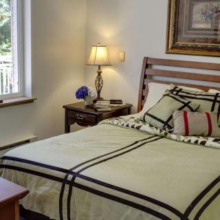 A cozy bedroom with a neatly made bed, bedside lamp, and a window providing natural light.