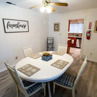 A cozy dining room with a white oval table set for four, featuring a 'family' wall art and ceiling fan.