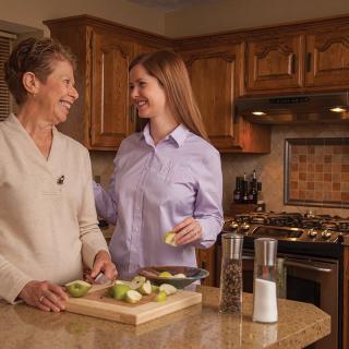 Two women smiling and preparing food together in the kitchen.