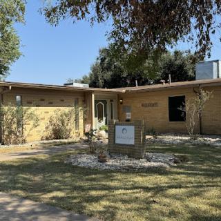 A charming single-story house with a well-maintained yard and clear blue skies.