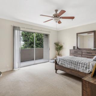 A spacious and well-lit bedroom featuring a bed, dresser, and a ceiling fan, with sliding doors leading to a balcony.