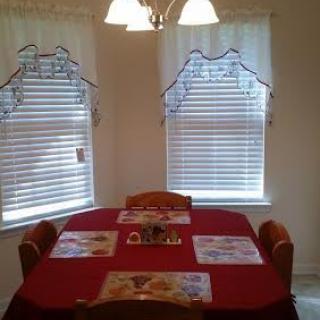 A cozy dining area with a red tablecloth and placemats, flanked by windows with decorative curtains.