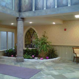 An indoor lobby with plants and seating, featuring a column and decorative arch window.