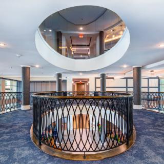 A modern interior with a circular balcony and intricate railing, illuminated by ceiling lights.
