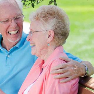 A joyful elderly couple smiling and sitting together on a bench outside.
