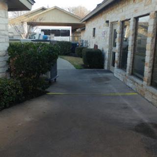 A view of a pathway beside a residential building, lined with shrubs.