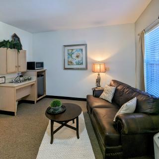 A cozy living room with a leather couch, round coffee table, and a kitchenette in the corner.