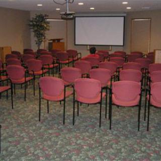 An empty conference room with arranged chairs facing a projector screen.