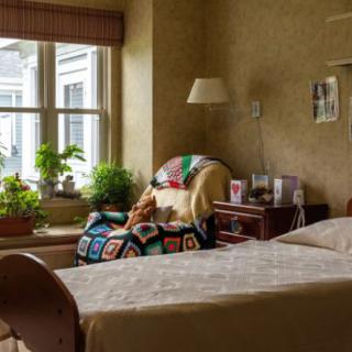 A cozy bedroom with a bed, chair, and potted plants by the window.