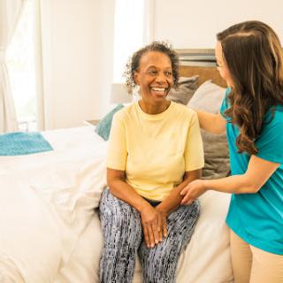 A caregiver sharing a joyful moment with an elderly woman in a comfortable bedroom setting.