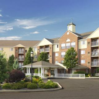 A large, multi-story residential building with landscaped surroundings under a clear blue sky.