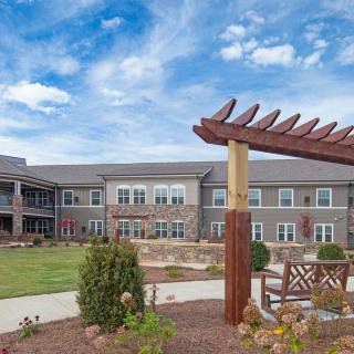 A modern building with a garden and pergola structure under a cloudy sky.