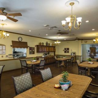 A cozy dining room with wooden tables and chairs, adorned with decorative plants and lit by elegant chandeliers.