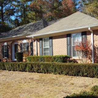 A brick suburban house with a neatly trimmed yard and surrounding trees.