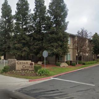 Entrance to an apartment complex surrounded by tall trees and marked with a sign.