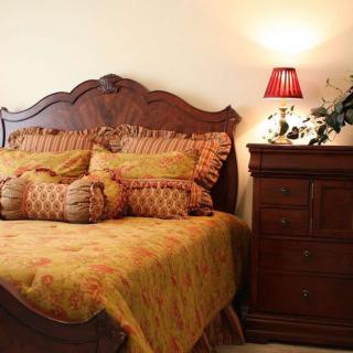 A cozy bedroom featuring a wooden bed with ornate pillows and a matching dresser, softly illuminated by a lamp.