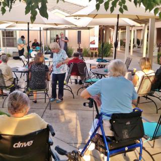 A group of elderly individuals enjoying an outdoor community event under patio umbrellas.