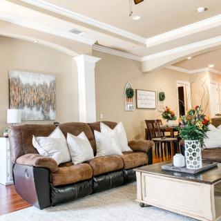 A cozy living room featuring a brown leather sofa with white pillows, a wooden coffee table adorned with plants, and artwork displayed on the walls.