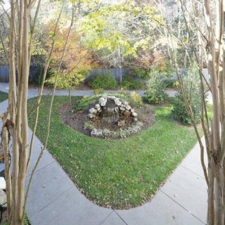 A serene garden with a central stone fountain surrounded by pathways and lush greenery.