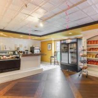 Interior view of a cozy cafe with a service counter, refrigerated drinks, and shelves stocked with products.