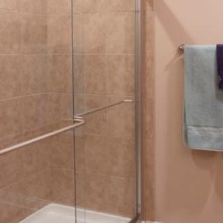 A bathroom with a tiled shower and glass door, featuring towels on the wall.