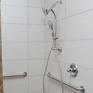 A tiled shower with a handheld showerhead and safety grab bars.