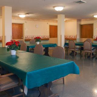 A spacious dining area featuring tables with green tablecloths and decorative flowers, ready for guests.