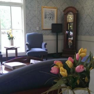 A cozy living room with a grandfather clock and floral arrangements.