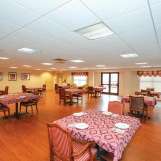 An empty dining hall with neatly arranged tables and chairs on a wooden floor.