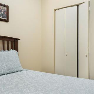 A small bedroom with a bed and closet, featuring a painting on the wall.